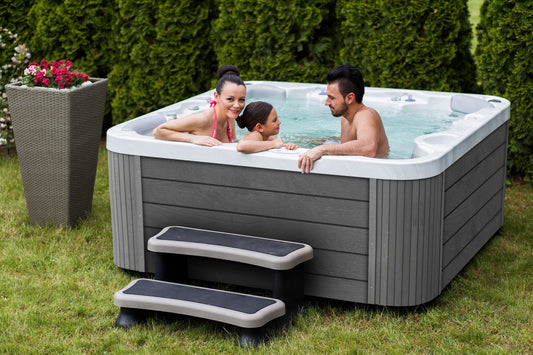 Couple relaxing in a modern hot tub on a backyard deck, surrounded by greenery β choosing a spa over a traditional pool for wellness and comfort.